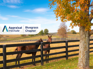 This photo depicts horses in a pasture fenced with black rails in a Kentucky landscape with the Appraisal Institute Bluegrass Chapter Logo