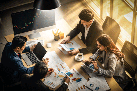 Work team sitting on a table looking of analytical charts and spreadsheets.