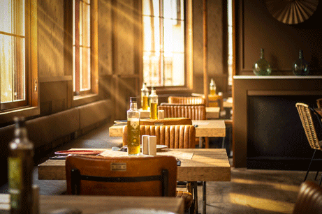 A restaurant interior with sunlight spilling in from the open windows into the dark wooded interior.
