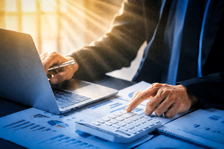 Business person using a calculator to calculate company financial figures from earnings papers, a businessman sitting in his office where the company financial chart is placed. Banner with copy space.