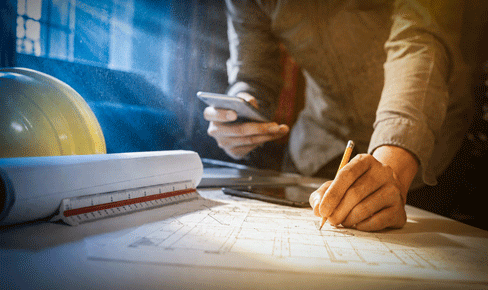 Business man hand working and laptop with on on architectural project at construction site at office desk 