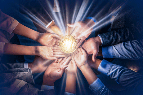 Cropped top view of group of business professionals forming circle with their hands, holding glowing light bulb together. Concept of teamwork, innovative solutions, collaboration and shared ideas.